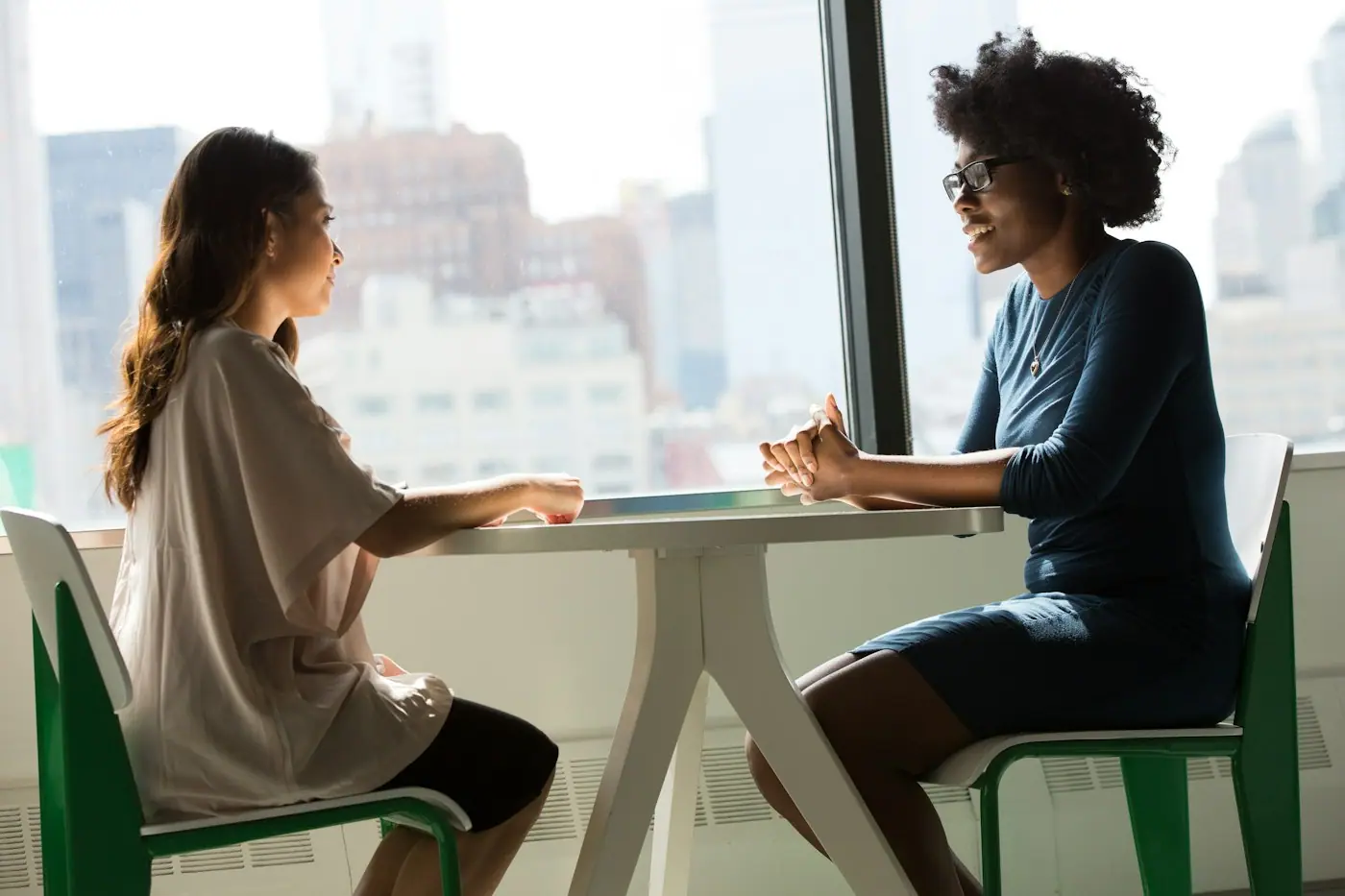 Dos personas conversando en una mesa junto a una ventana